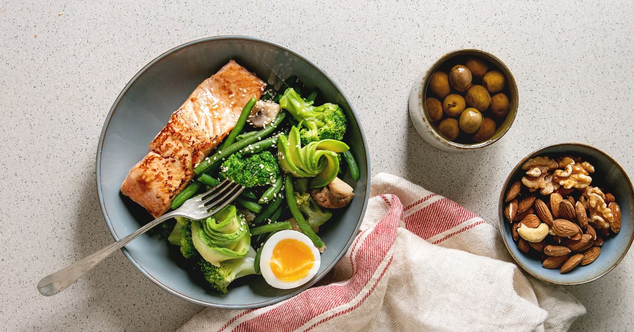 A healthy meal for managing PCOS with grilled salmon, green vegetables, and a soft-boiled egg. Side dishes include green olives and mixed nuts (almonds, walnuts, cashews).