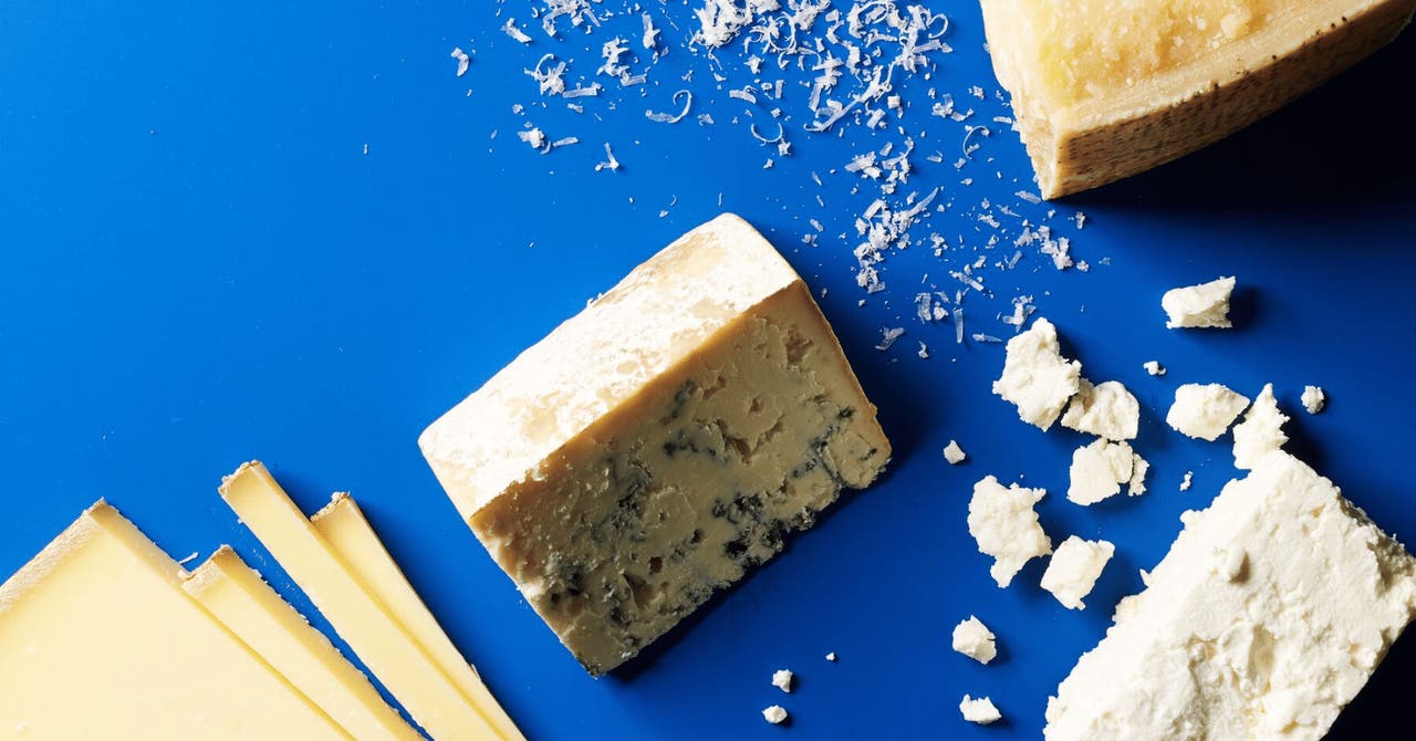 Various types of cheese on a bright blue background, featuring both hard and crumbly varieties.