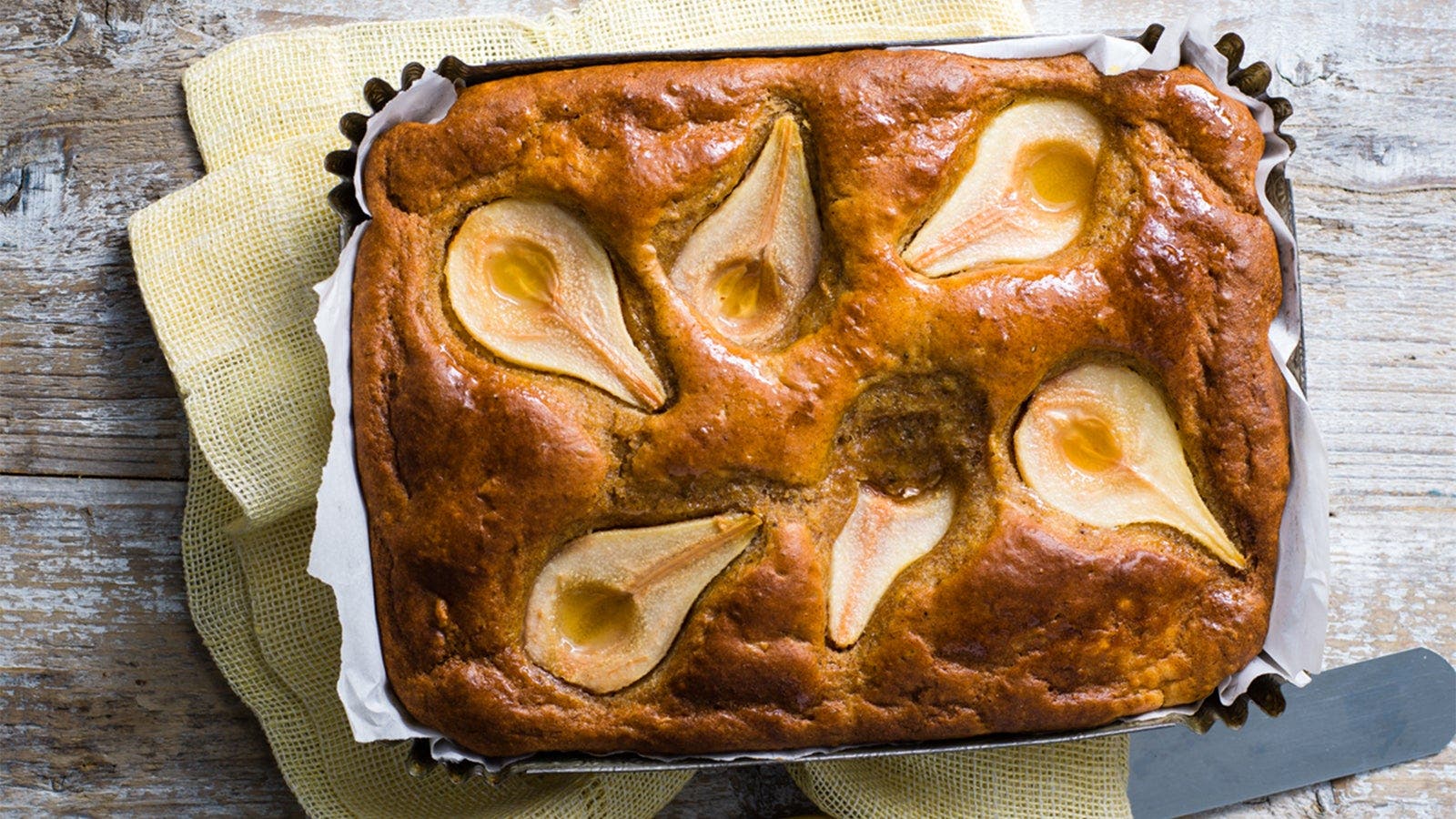 A pear and ginger loaf cake with whole pear halves baked into the top, presented in a baking tray lined with baking paper.