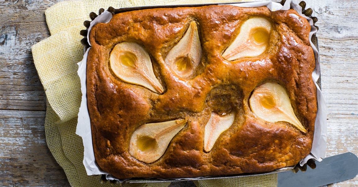 A pear and ginger loaf cake with whole pear halves baked into the top, presented in a baking tray lined with baking paper.