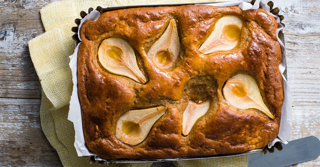 A pear and ginger loaf cake with whole pear halves baked into the top, presented in a baking tray lined with baking paper.