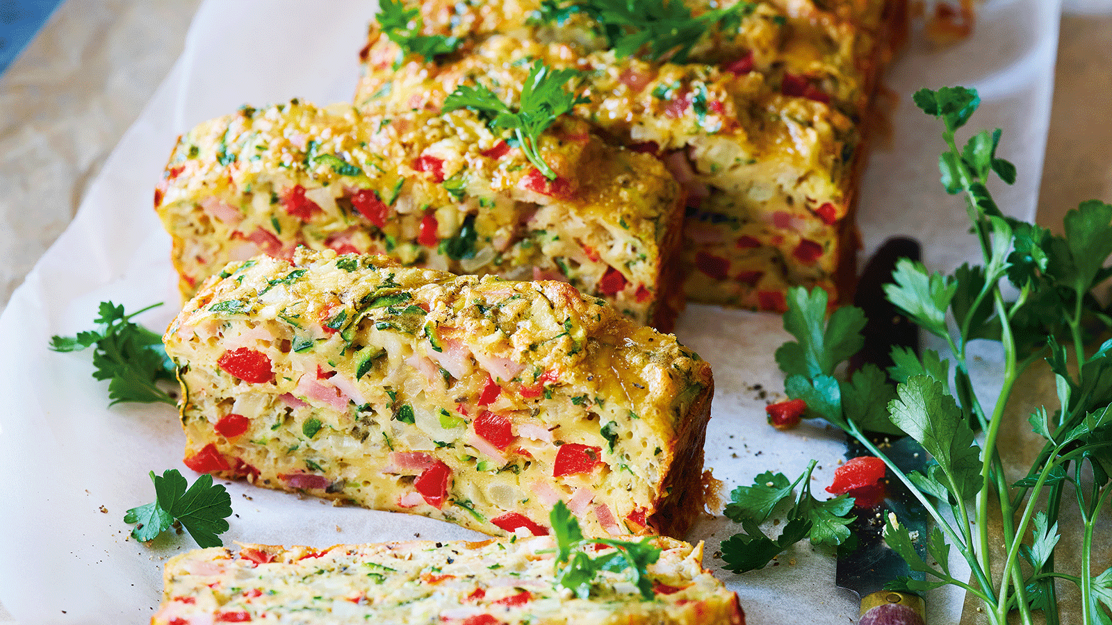Close-up of a colourful vegetable loaf sliced on a white surface, garnished with fresh parsley.