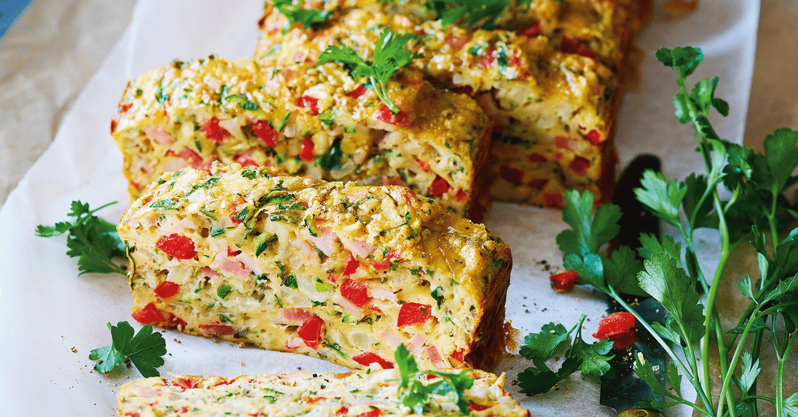 Close-up of a colourful vegetable loaf sliced on a white surface, garnished with fresh parsley.