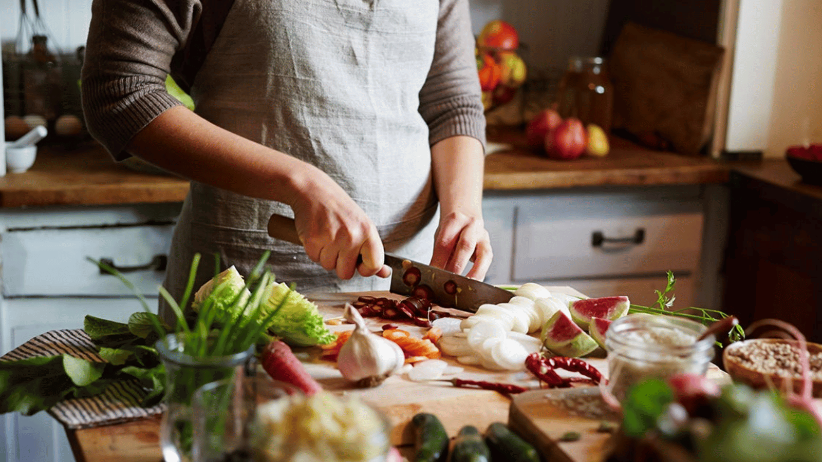 Person chopping fresh vegetables including onions, lettuce, and radishes on a wooden kitchen counter, surrounded by various ingredients.