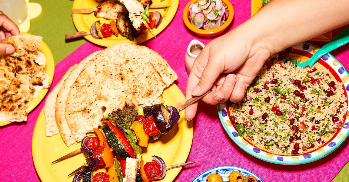 Colourful table spread with skewered vegetables, couscous salad, and flatbreads.