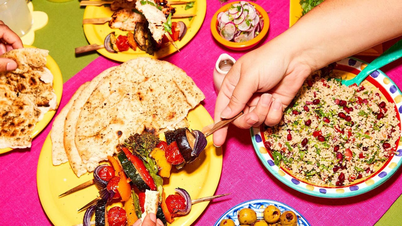 Colourful table spread with skewered vegetables, couscous salad, and flatbreads.