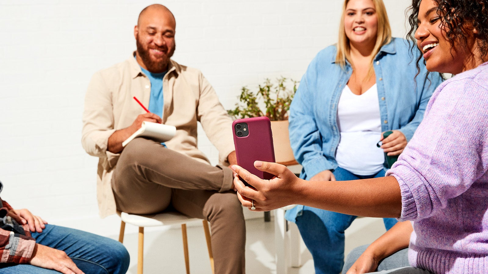 Group of people smiling and looking at a smartphone during a casual meeting.