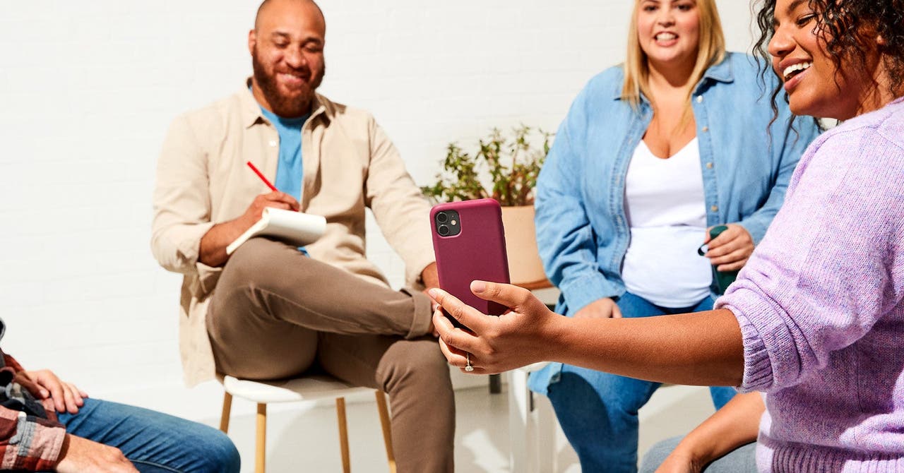 Group of people smiling and looking at a smartphone during a casual meeting.
