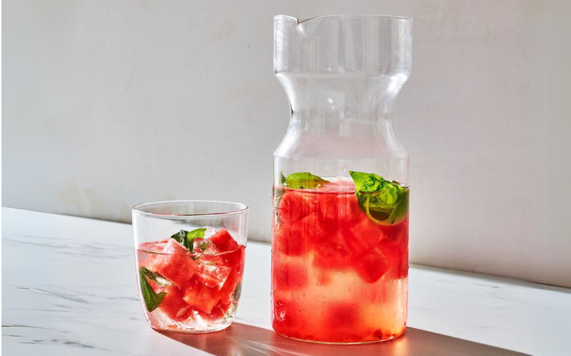  A pitcher and glass filled with watermelon and mint-infused water, placed on a white marble surface with a light background.