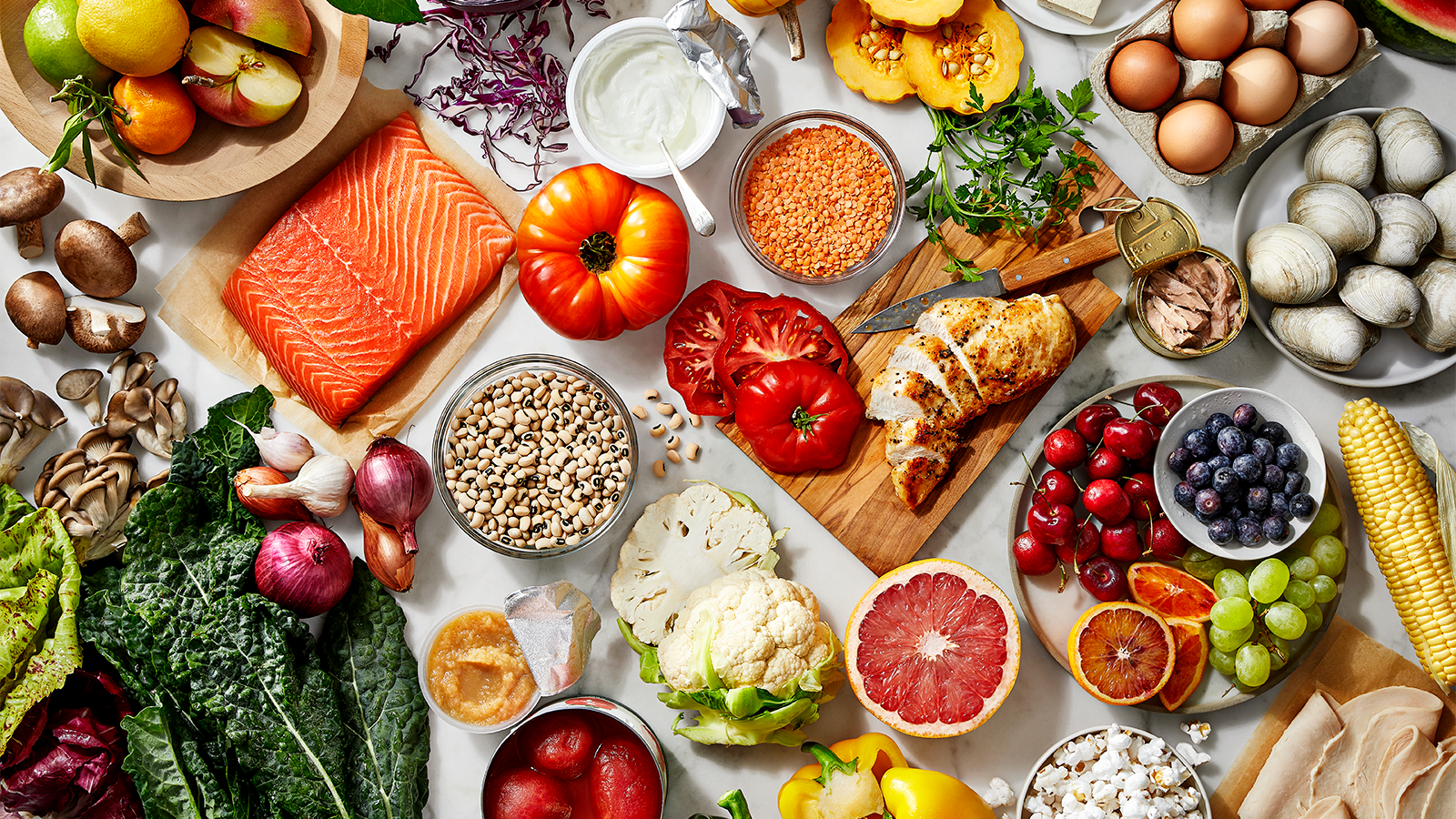 An assortment of healthy foods including fresh fruits, vegetables, salmon, chicken, legumes, grains, and dairy products.