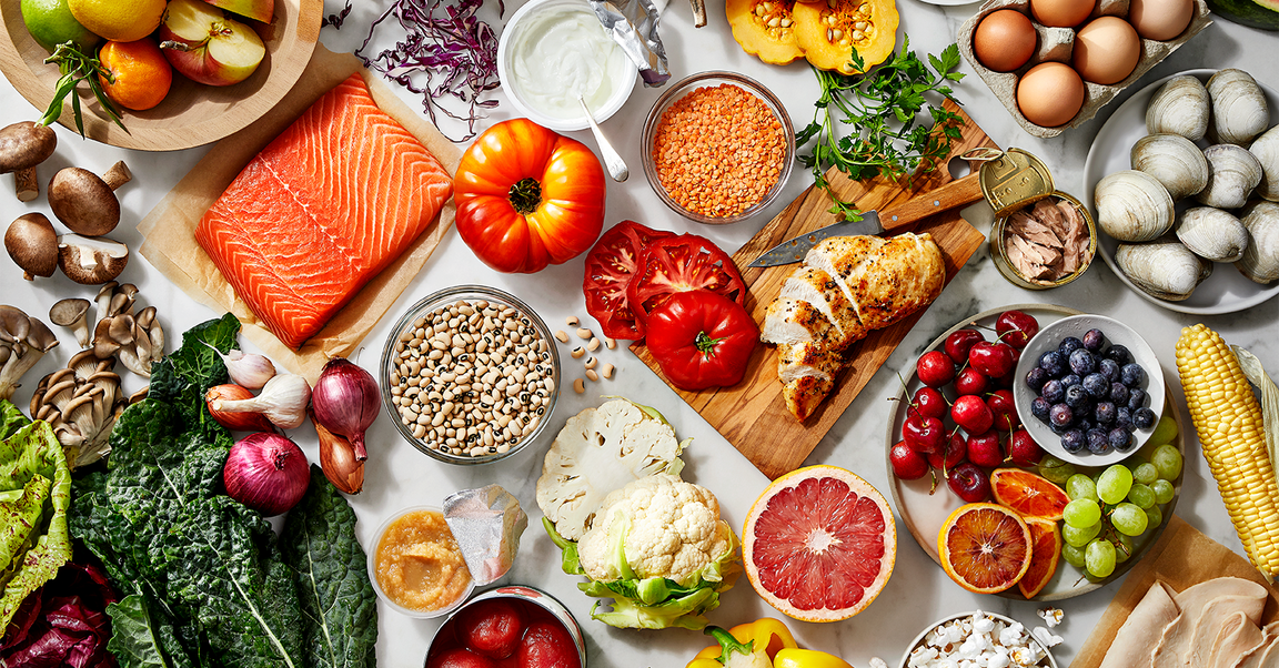 An assortment of healthy foods including fresh fruits, vegetables, salmon, chicken, legumes, grains, and dairy products.