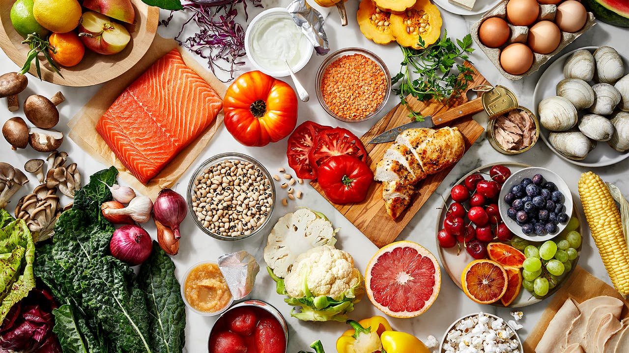 An assortment of healthy foods including fresh fruits, vegetables, salmon, chicken, legumes, grains, and dairy products.