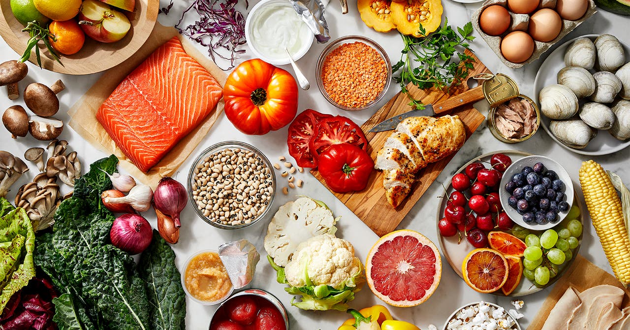 An assortment of healthy foods including fresh fruits, vegetables, salmon, chicken, legumes, grains, and dairy products.