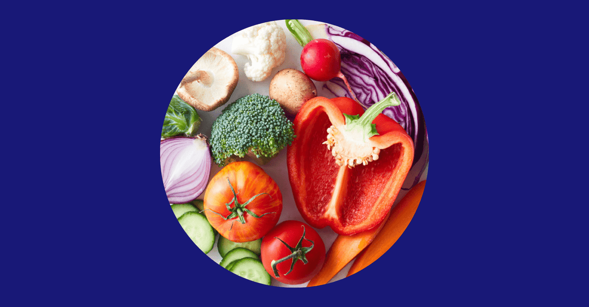 A variety of fresh vegetables including red bell pepper, broccoli, tomato, cucumber, mushrooms, and red onion arranged in a circle on a blue background.