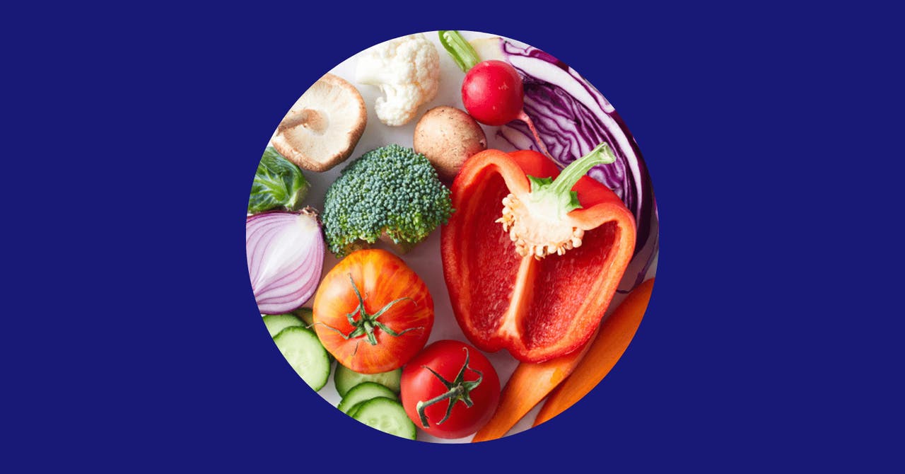 A variety of fresh vegetables including red bell pepper, broccoli, tomato, cucumber, mushrooms, and red onion arranged in a circle on a blue background.