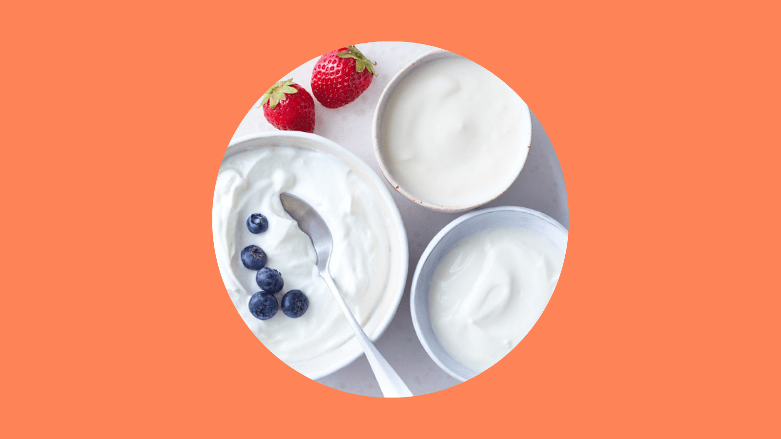 Bowl of creamy yoghurt topped with fresh blueberries, accompanied by whole strawberries, served in ceramic bowls.