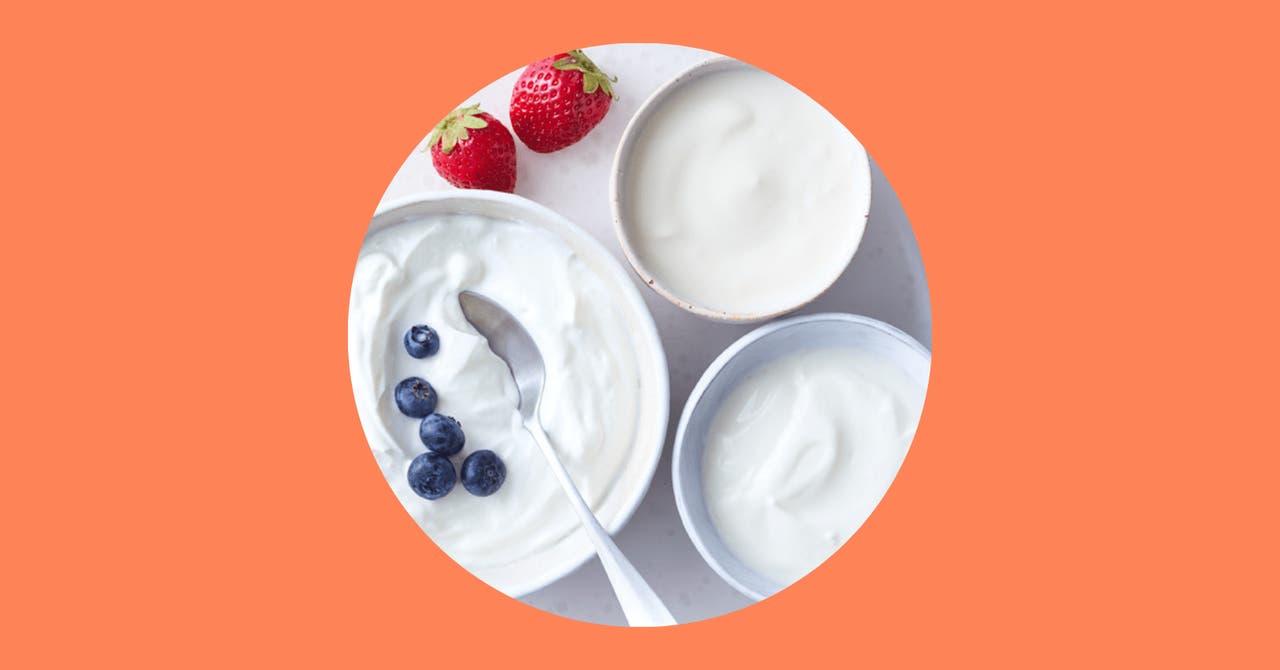 Bowl of creamy yoghurt topped with fresh blueberries, accompanied by whole strawberries, served in ceramic bowls.