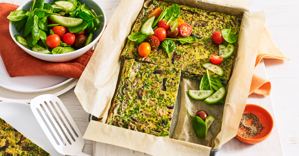 Baked vegetable slice served on parchment paper with fresh spinach, cherry tomatoes, and cucumber salad