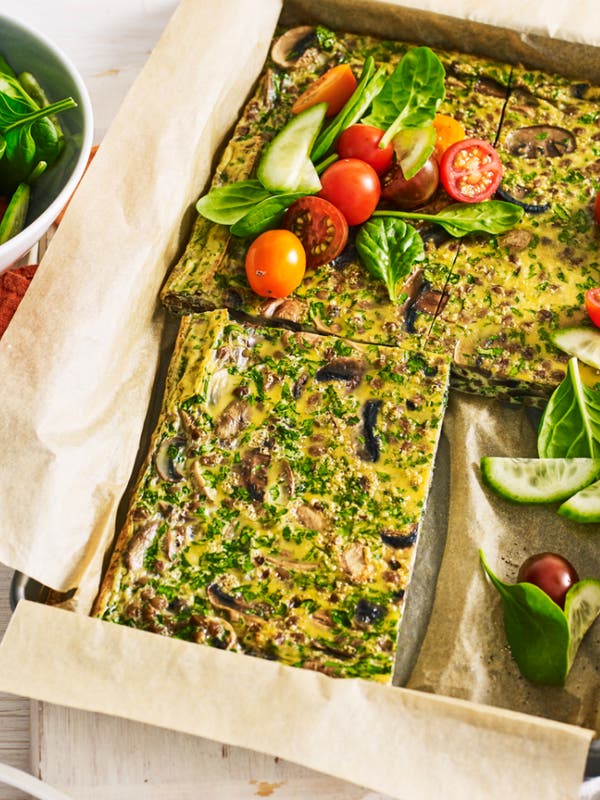 Baked vegetable slice served on parchment paper with fresh spinach, cherry tomatoes, and cucumber salad