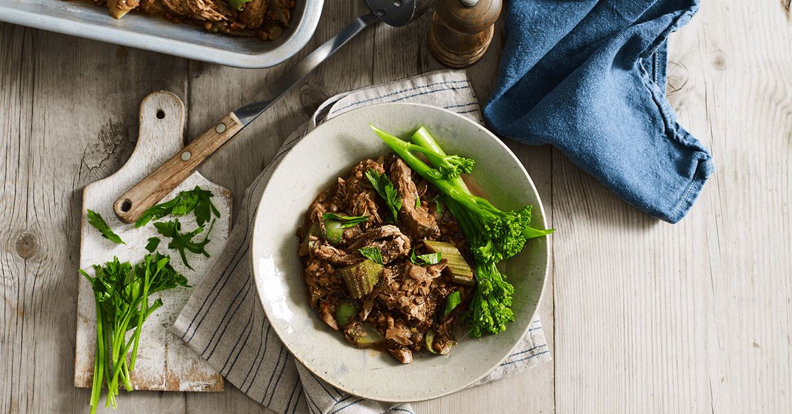 A delicious dish with shredded meat, vegetables, and green broccolini on a white plate, garnished with fresh herbs.