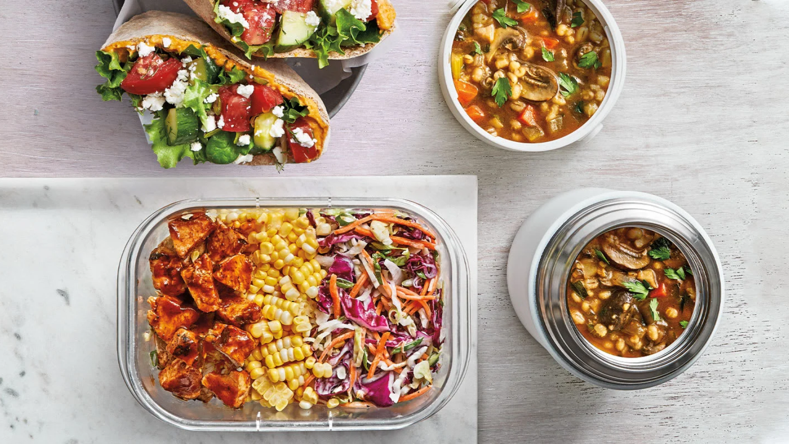 An assortment of healthy meals including wraps with vegetables and feta, a container with sweet potatoes, corn, and coleslaw, and two containers of vegetable soup.