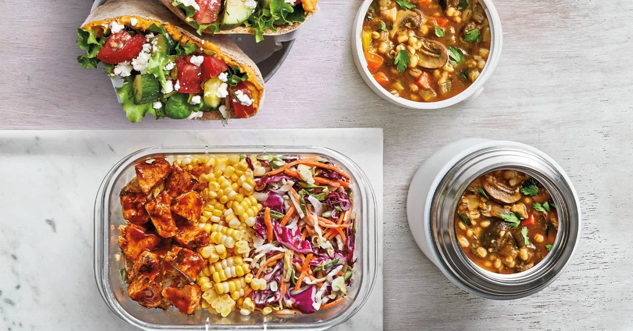An assortment of healthy meals including wraps with vegetables and feta, a container with sweet potatoes, corn, and coleslaw, and two containers of vegetable soup.