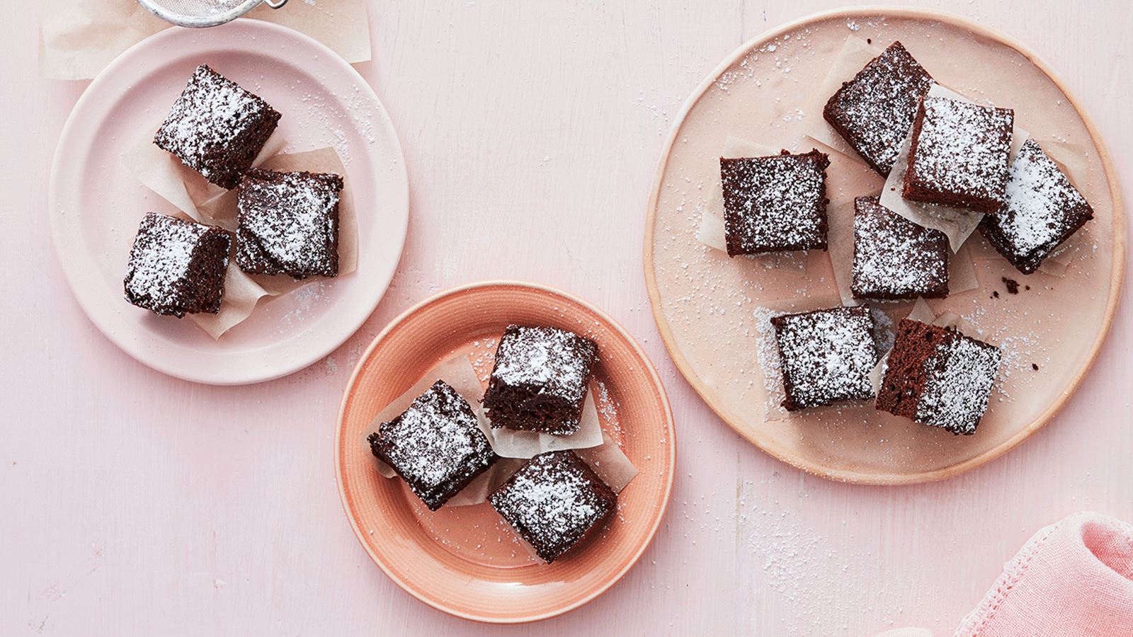 Delicious homemade chocolate brownies dusted with powdered sugar, arranged on pink and beige plates.