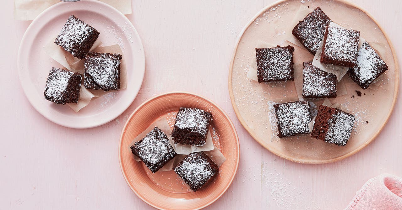 Delicious homemade chocolate brownies dusted with powdered sugar, arranged on pink and beige plates.