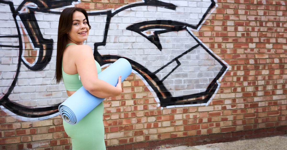 Vrouw in sportkleding met een yogamatje onder haar arm