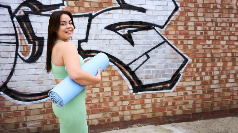 Vrouw in sportkleding met een yogamatje onder haar arm