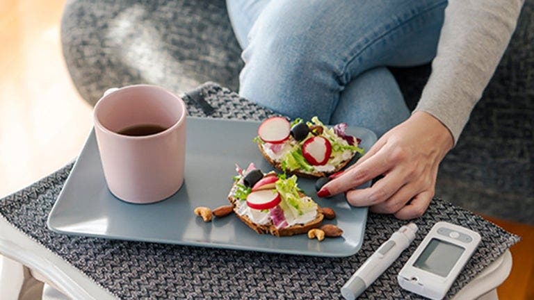 Ein Frühstücksteller mit belegtem Brot und Kaffee, daneben liegt das Blutzuckermessgerät.