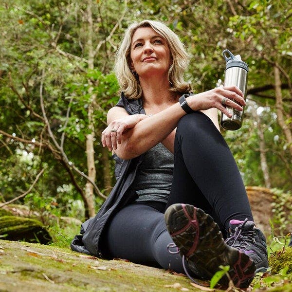 Blonde Frau sitzt in Sportkleidung auf einem Waldboden