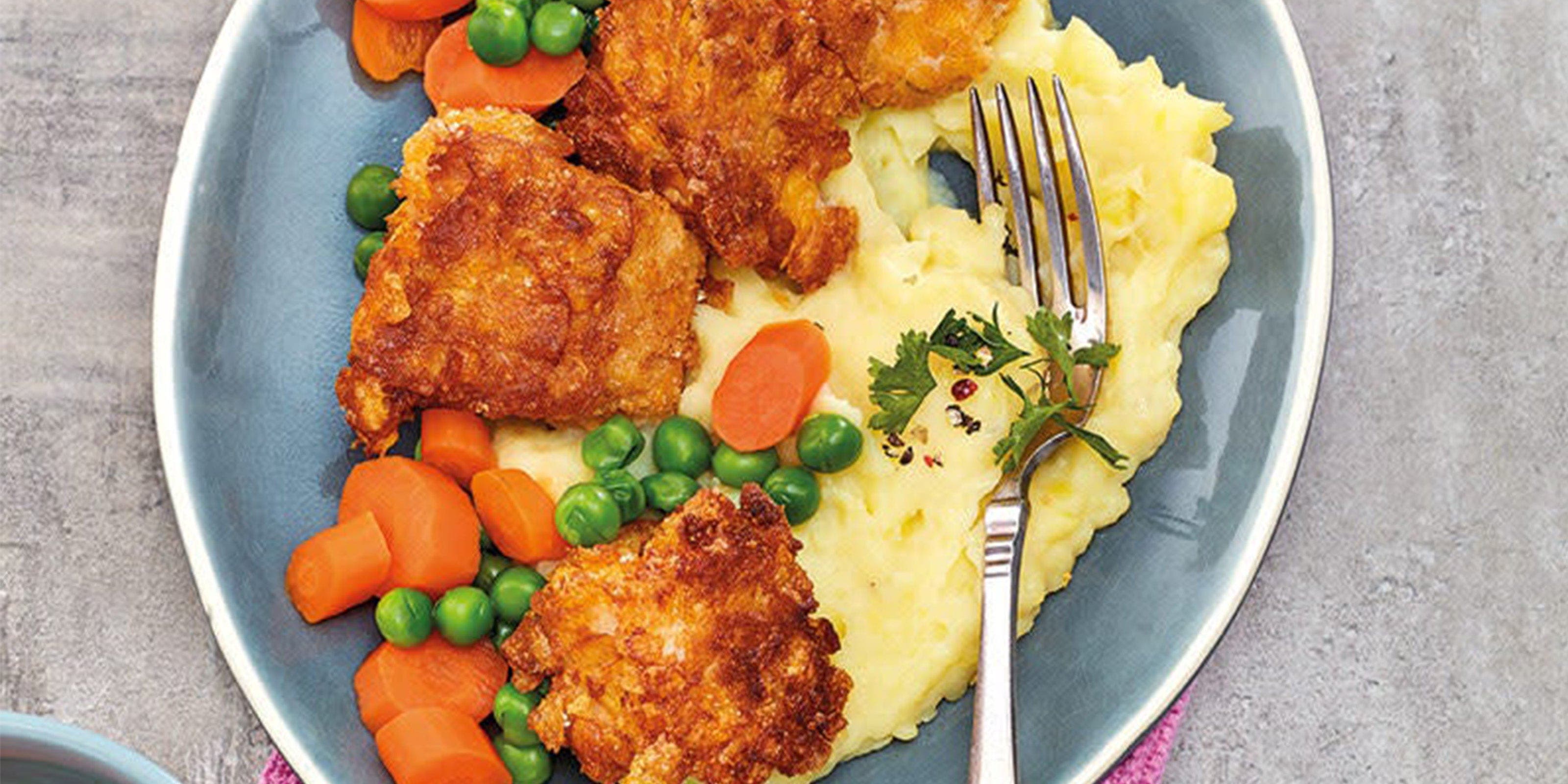 Une assiette avec des nuggets de poisson, de la purée de pommes de terre et des légumes mélangés