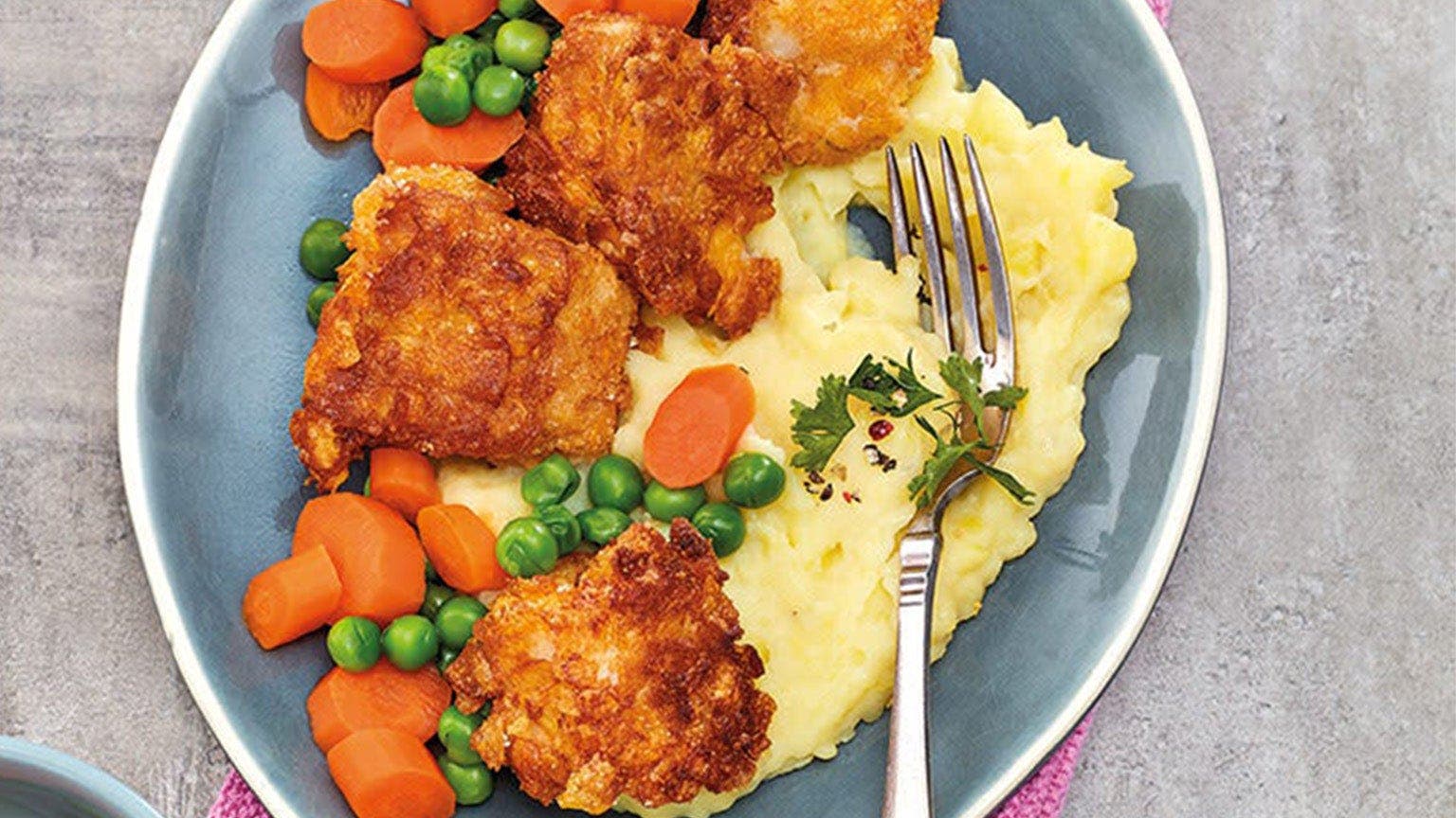 Une assiette avec des nuggets de poisson, de la purée de pommes de terre et des légumes mélangés