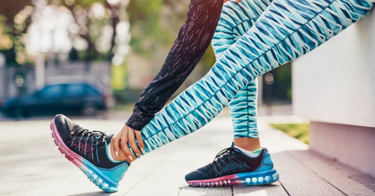 Eine Frau in bunter Sportkleidung dehnt ihre Beine