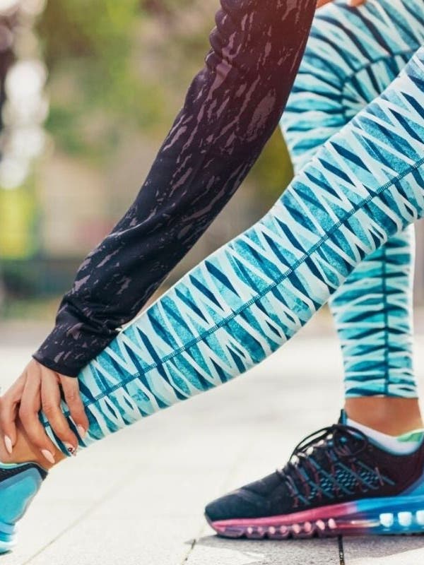 Eine Frau in bunter Sportkleidung dehnt ihre Beine