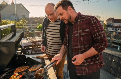 Zwei Männer grillen draußen auf einer Dachterrasse