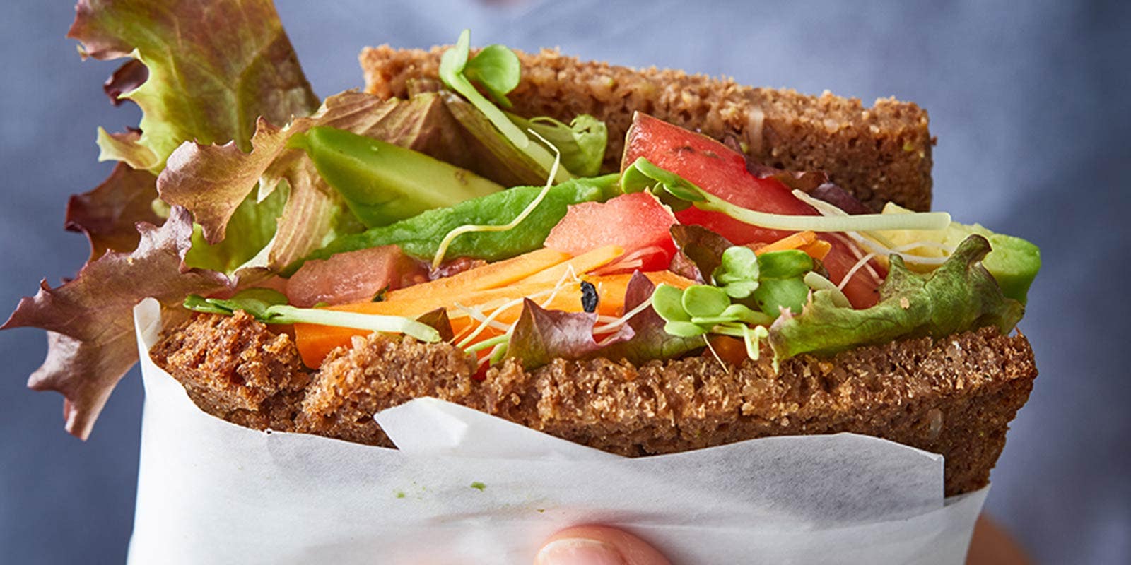 Eine Frau hält ein Vollkornbrot in der Hand, belegt mit Salat, Tomate, Avocado und Co.