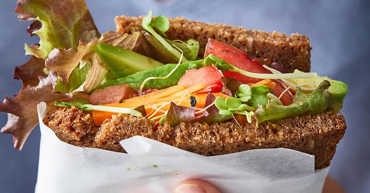 Eine Frau hält ein Vollkornbrot in der Hand, belegt mit Salat, Tomate, Avocado und Co.
