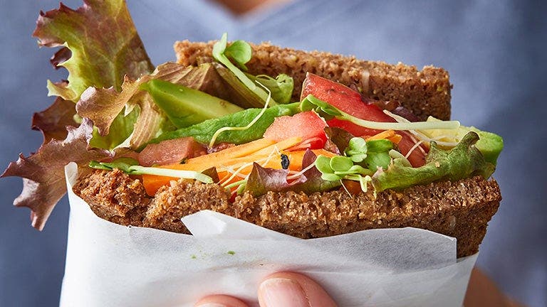 Eine Frau hält ein Vollkornbrot in der Hand, belegt mit Salat, Tomate, Avocado und Co.