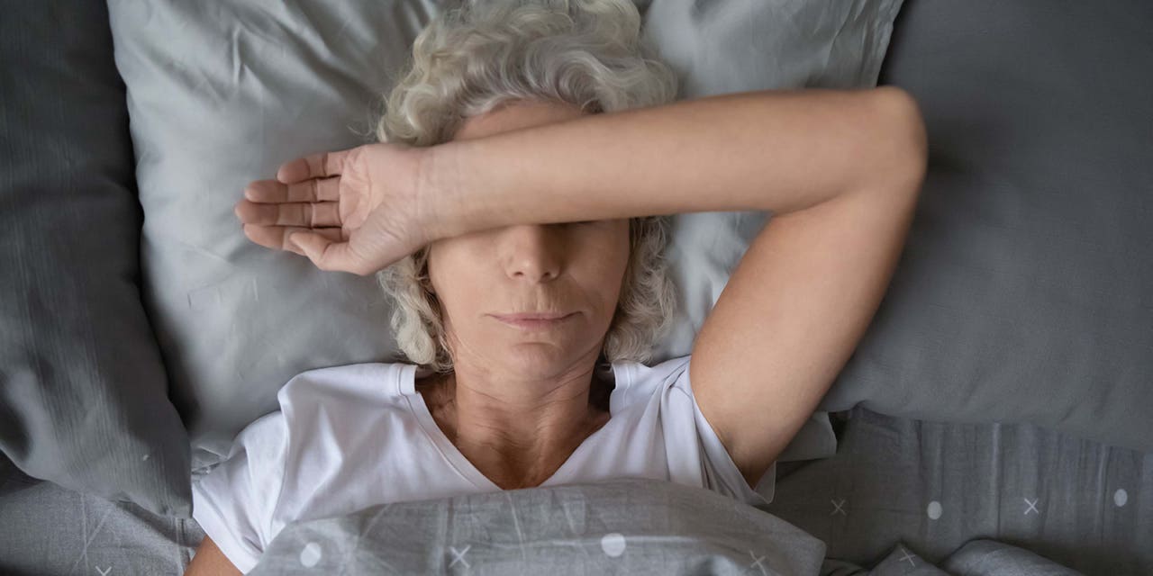Une femme couchée dans le lit, les bras croisés sur le visage
