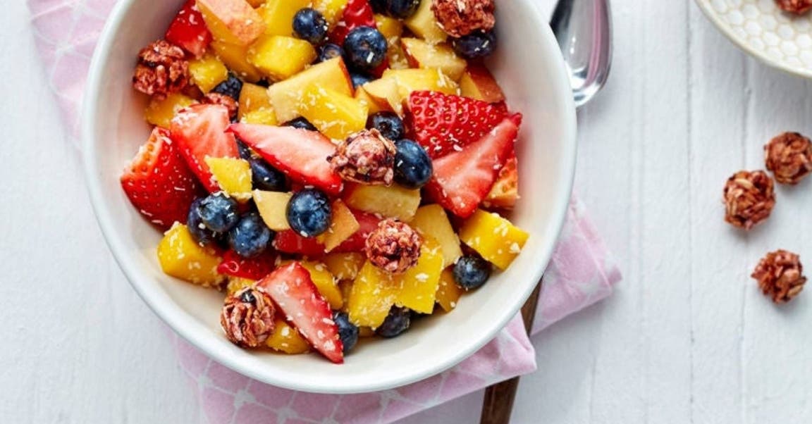 Un bol de salade de fruits contenant de la mangue, des fraises, des myrtilles et des céréales