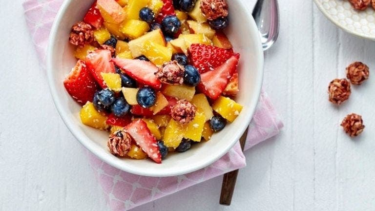 Un bol de salade de fruits contenant de la mangue, des fraises, des myrtilles et des céréales