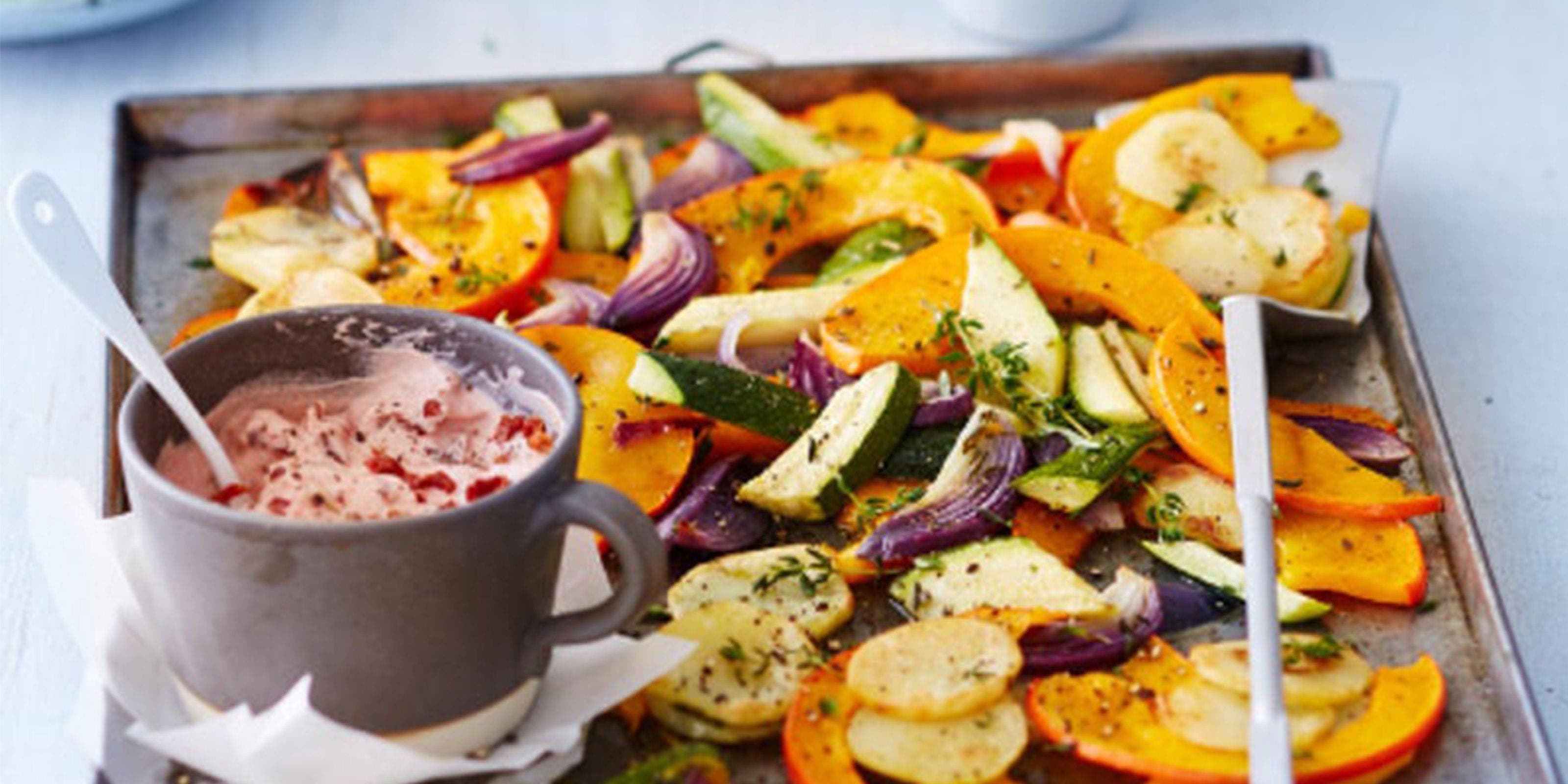 Ein Blech mit Kürbisspalten, anderem Ofengemüse und einem Tomaten-Dip