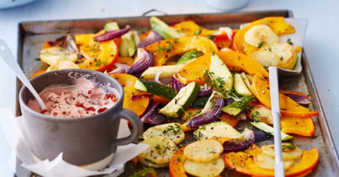 Ein Blech mit Kürbisspalten, anderem Ofengemüse und einem Tomaten-Dip
