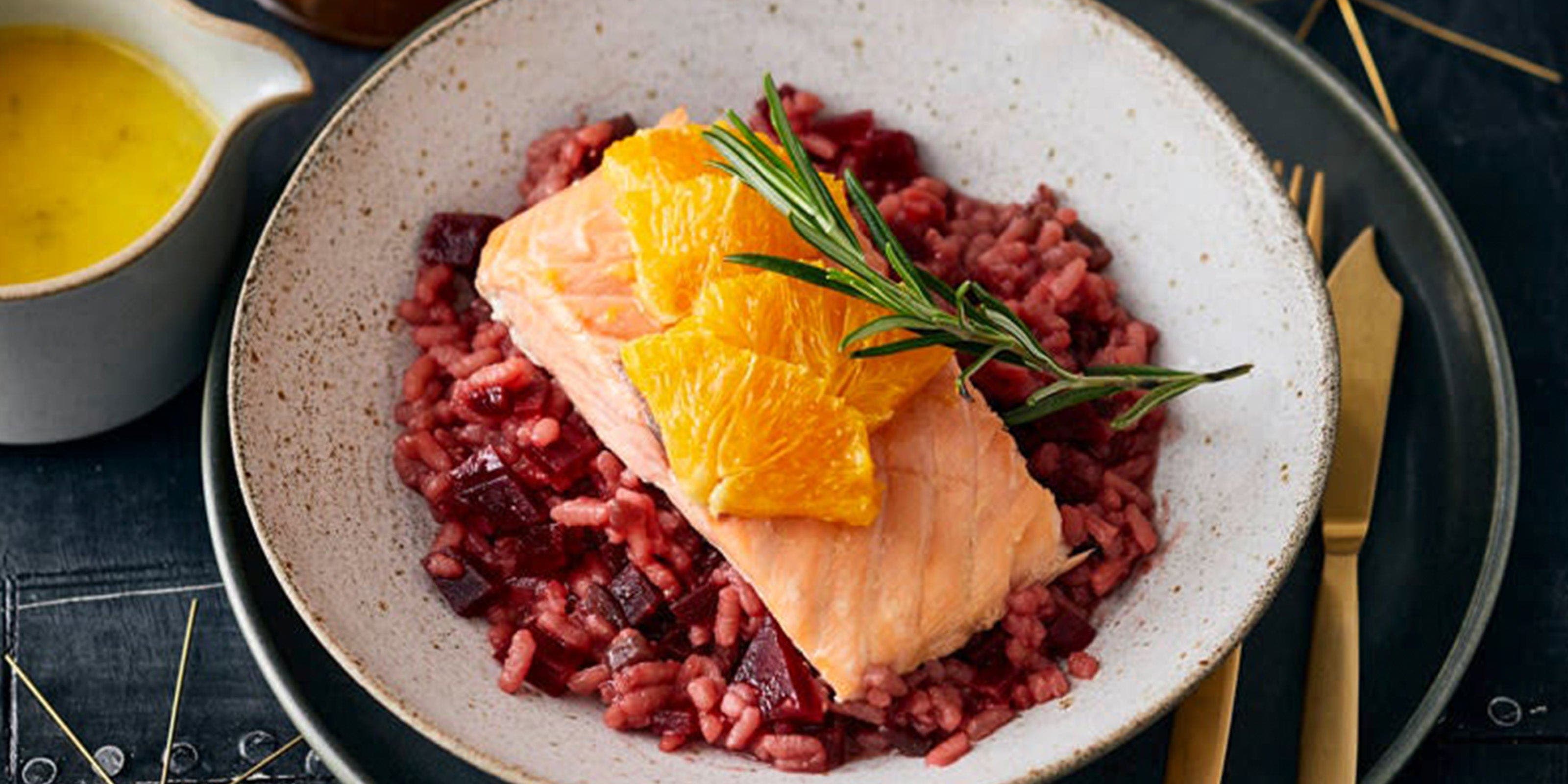 Ein Teller mit Rote-Bete-Risotto und Lachs. Link daneben ein Kännchen mit Orangensauce.