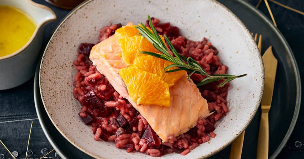 Ein Teller mit Rote-Bete-Risotto und Lachs. Link daneben ein Kännchen mit Orangensauce.