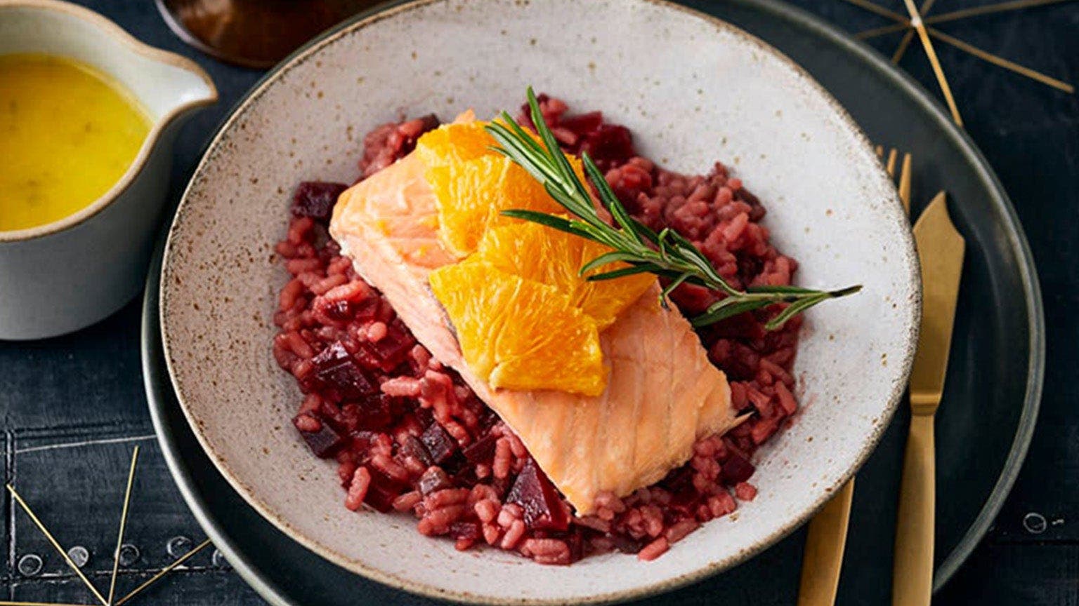 Ein Teller mit Rote-Bete-Risotto und Lachs. Link daneben ein Kännchen mit Orangensauce.