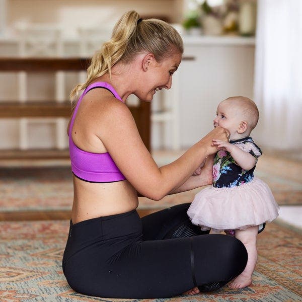 Blonde Frau in Sportkleidung lacht ihr Baby an
