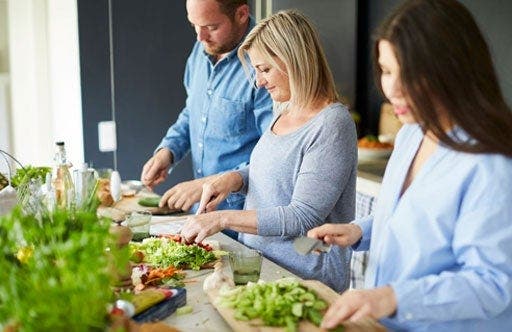 Deux femmes et un homme coupent des légumes